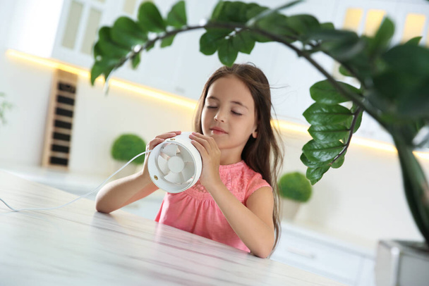 Little girl enjoying air flow from portable fan at home. Summer heat - Photo, image