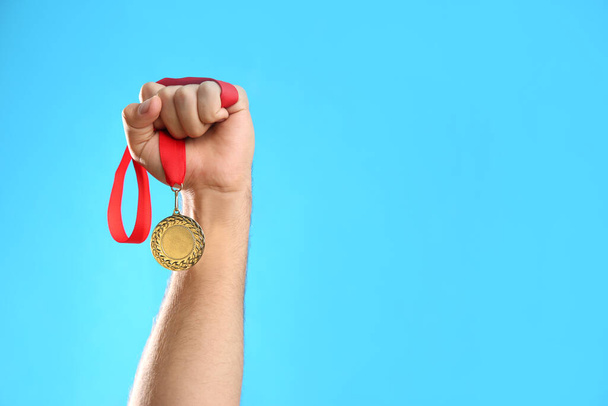 Man holding golden medal on light blue background, closeup. Space for design - Foto, Bild