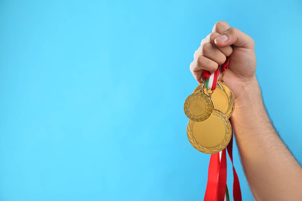 Man holding golden medals on light blue background, closeup. Space for design - Photo, Image