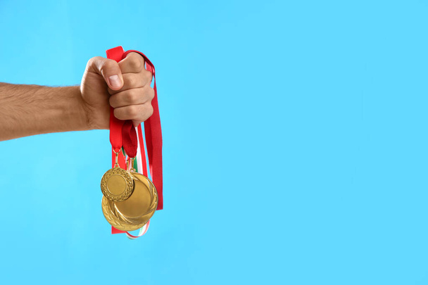 Man holding golden medals on light blue background, closeup. Space for design - 写真・画像