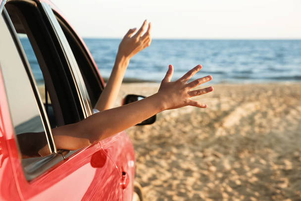 Woman and her daughter waving from car on beach, closeup. Summer trip - 写真・画像