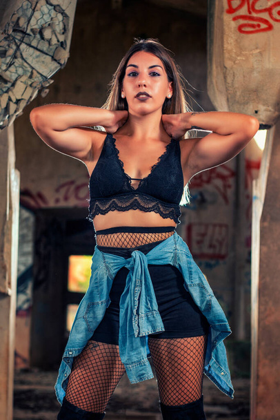 Young girl posing in a fashion way on an abandoned factory building using a blue denim shirt, black top and short jeans. - Foto, Bild