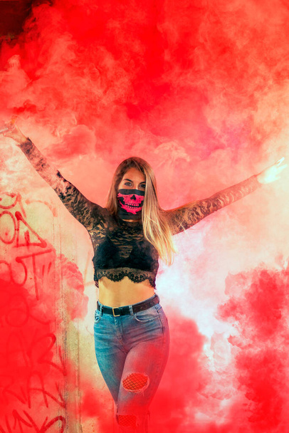 Chica peligrosa con máscara de boca rosa en una fábrica abandonada usando una granada de humo. - Foto, Imagen