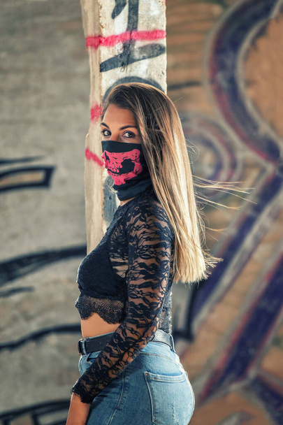 Gefährliches Mädchen mit pinkfarbener Mundmaske auf einem alten Sofa in einer verlassenen Fabrik. - Foto, Bild