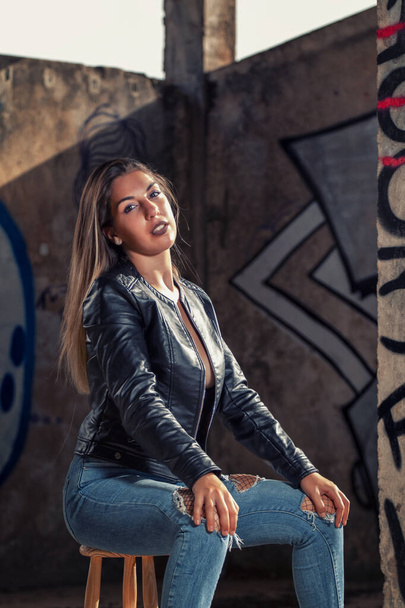 Model with leather jacket and blue jeans on a abandoned factory on sensual poses. - Photo, Image