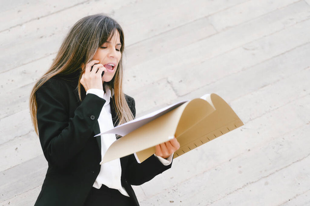 Boze zakenvrouw met documenten met behulp van mobiele telefoon en schreeuwen. - Foto, afbeelding