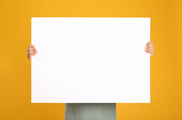 Man holding white blank poster on yellow background. Mockup for design - Φωτογραφία, εικόνα
