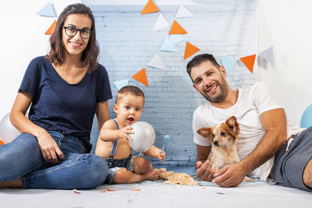 レンガの壁紙で構成されたセットで1年間の赤ちゃんの男の子のためのパーティーで息子と遊ぶ両親. - 写真・画像
