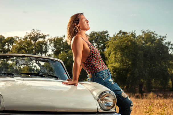 Женщина с белым кабриолетом винтажный автомобиль на сельской местности, в позе модного образа жизни. - Фото, изображение