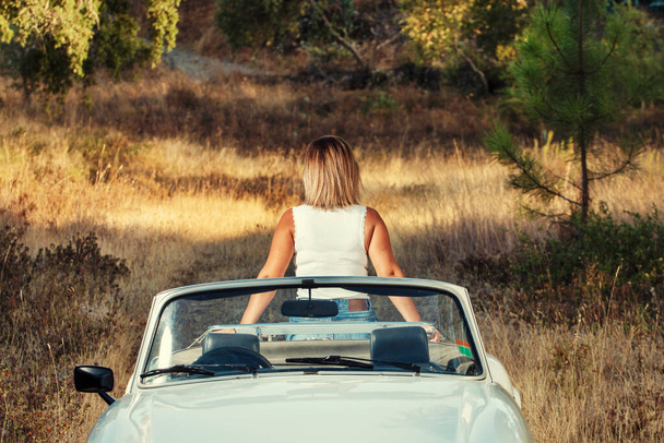Kobieta z białym, kabrioletowym samochodem na wsi, w pozowaniu modny styl życia. - Zdjęcie, obraz