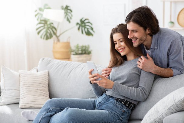 Positives junges Paar nutzt Handy zu Hause - Foto, Bild