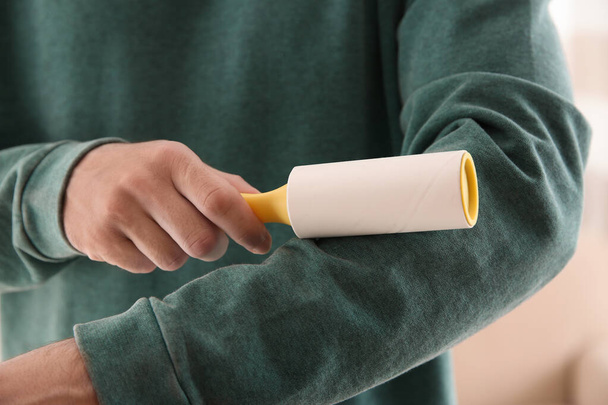 Man cleaning green sweatshirt with lint roller on light background, closeup - Foto, afbeelding
