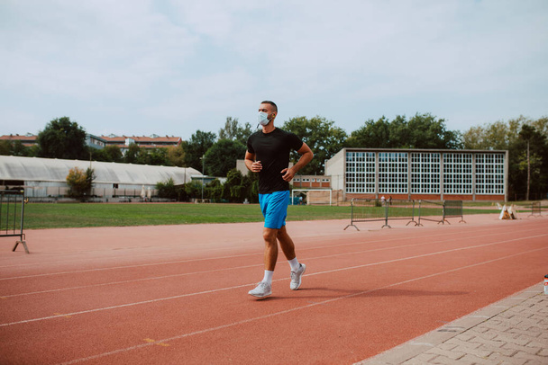 Egy fiatal kaukázusi atléta arcmaszkos képét egy versenypályán. A sprinter atlétikai futópályán fut. COVID - 19 koronavírus elleni védelem - Fotó, kép