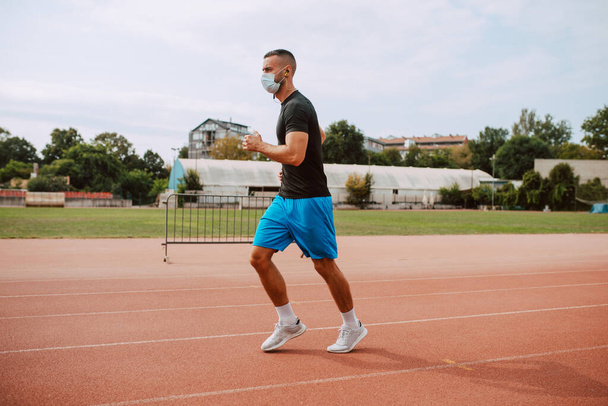 Знімок молодого чоловіка кавказького спортсмена з тренуванням маски для обличчя на гоночній трасі. Спринтер працює на спортивній біговій доріжці. COVID - 19 захист від коронавірусу
 - Фото, зображення