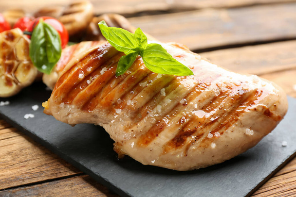 Tasty grilled chicken fillet with green basil on wooden table, closeup - Photo, image