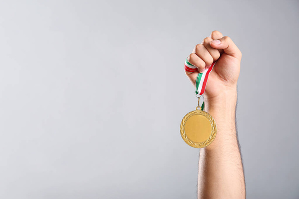 Man holding golden medal on grey background, closeup. Space for design - Zdjęcie, obraz