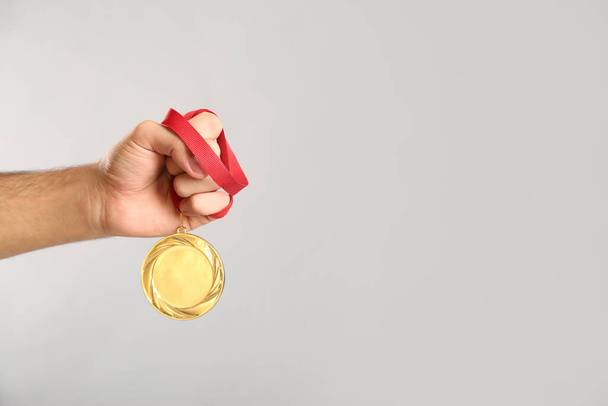 Man holding golden medal on grey background, closeup. Space for design - Foto, afbeelding