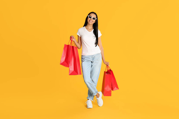 Beautiful young woman with paper shopping bags on yellow background - Foto, Imagen