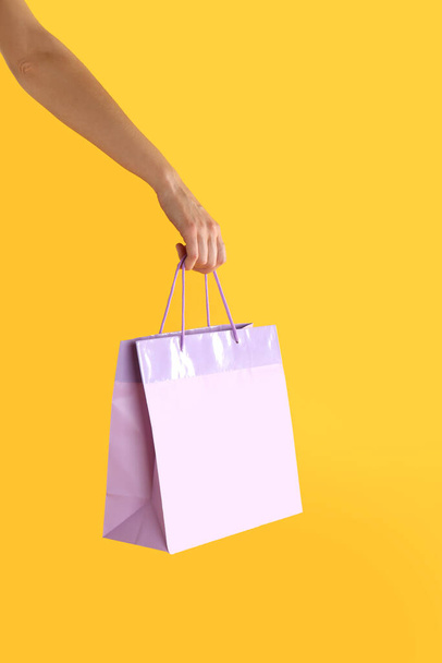 Woman with paper shopping bag on yellow background, closeup - Foto, imagen