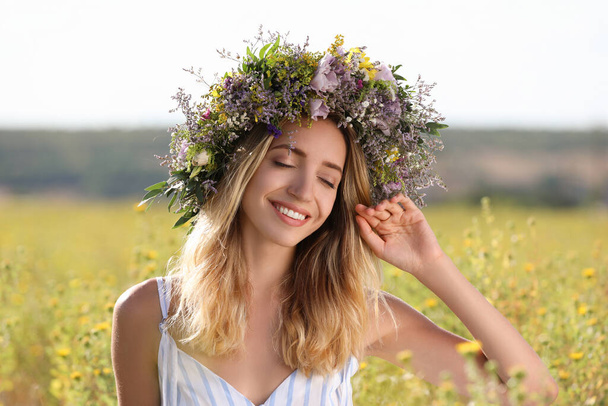 Young woman wearing wreath made of beautiful flowers in field on sunny day - Foto, immagini