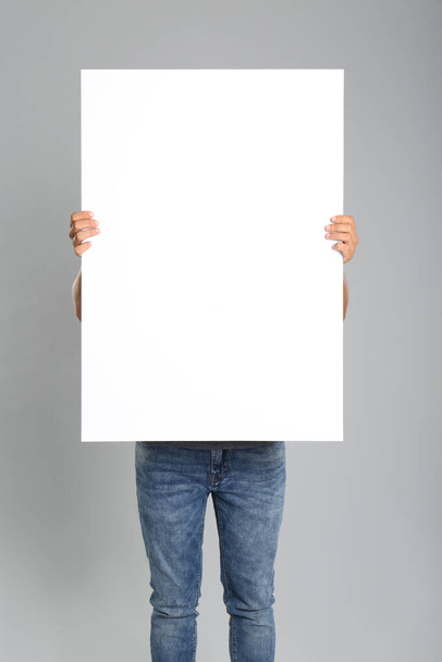 Man holding white blank poster on grey background. Mockup for design - Foto, immagini