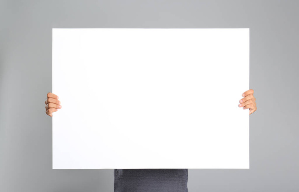 Man holding white blank poster on grey background. Mockup for design - Фото, изображение