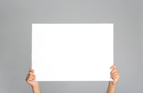 Man holding white blank poster on grey background, closeup. Mockup for design - Photo, image