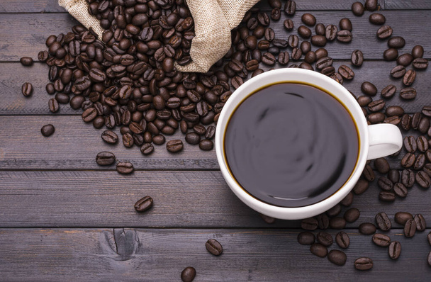 Ciemna kawa w białej filiżance kawy i palone ziarna kawy umieszczone na czarnym drewnianym stole i jest miejsce na projekt tekstu. - Zdjęcie, obraz