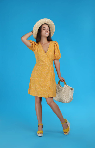 Young woman wearing dress with straw bag on light blue background - Photo, image