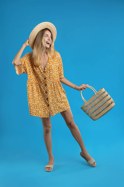 Young woman wearing stylish dress with straw bag on blue background - Photo, image