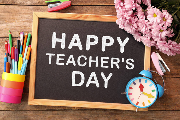 Kis tábla szöveggel Happy Teacher 's Day, írószerek és virágok fa asztalon, felülnézet - Fotó, kép
