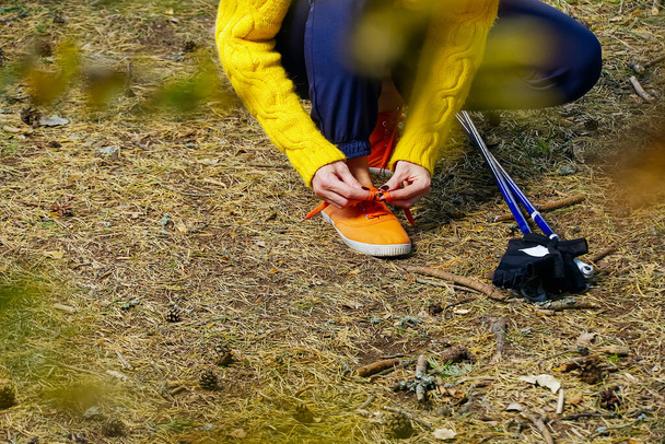 Sporty hiking woman tying shoelaces on her jogging shoes while taking a break after hiking in autumn forest. hiking concept, healthy outdoor lifestyle. - Photo, Image