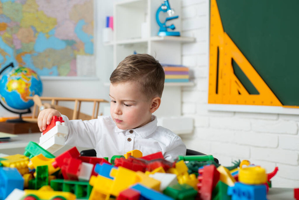 Toddler child boy playing with toys developing and learning activities. Cute child is sitting at a desk indoors. Child of primary school. Concept of education and reading. - Foto, Imagen