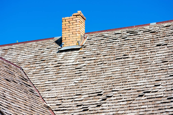 Вид на традиционную деревянную черепичную крышу с несколькими смазанными тряпками. Поврежденный кирпичный дымоход. - Фото, изображение