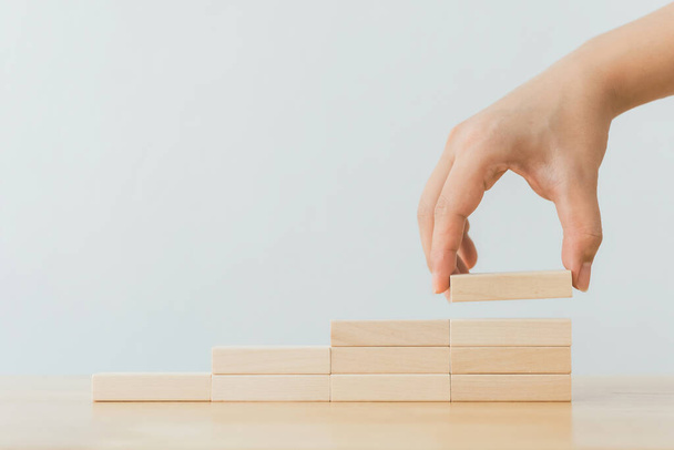 Hand arranging wood block stacking as step stair. Ladder career path concept for business growth success process - 写真・画像