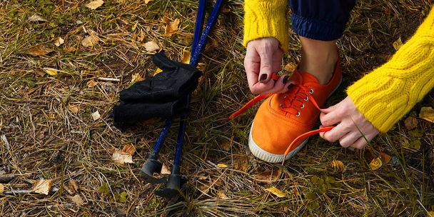 秋の森をハイキングした後に休憩を取りながら、ジョギングシューズに靴ひもを結ぶスポーティハイキング女性。ハイキングのコンセプト健康的なアウトドアライフスタイル. - 写真・画像