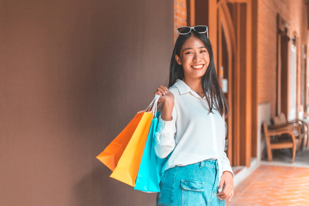 Genç Asyalı kadınlar alışveriş merkezinde ya da alışveriş merkezinde alışveriş yapmak için renkli alışveriş torbaları taşırlar. İndirim günü, mutlu alışveriş konsepti..  - Fotoğraf, Görsel
