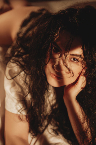 Beautiful woman with black wavy hairs lying on bed - Fotoğraf, Görsel