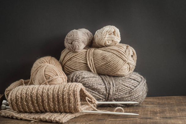 Earthy tones of yarn skeins. Home hobby, cozy knitted. Yarn on a wooden table on a black background. - Photo, Image