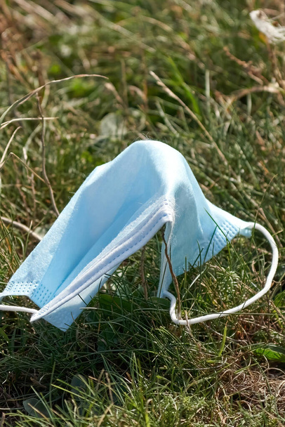 Використана одноразова блакитна маска для обличчя недбало викинута на траву під час пандемії Ковіда-19
. - Фото, зображення