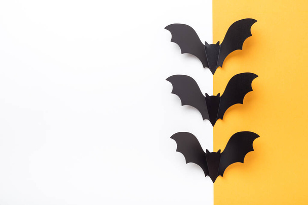 Halloween decorations. Black paper bats on yellow and white background. Halloween concept. Flat lay, top view, copy space - Image - Foto, immagini