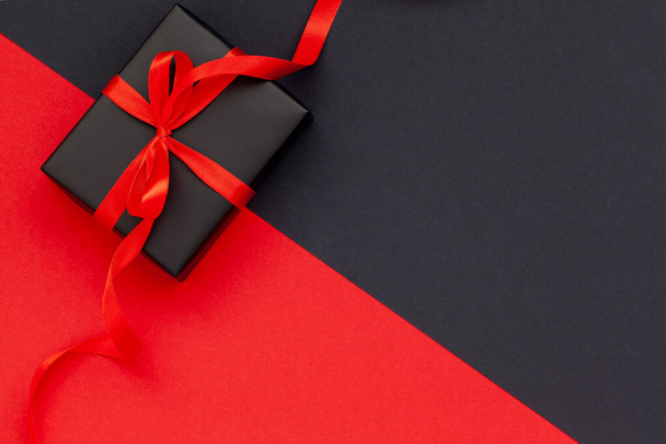 Concept Black Friday. Vue du dessus de la boîte cadeau noire avec ruban rouge sur fond noir et rouge avec espace de copie pour le texte. - Photo, image