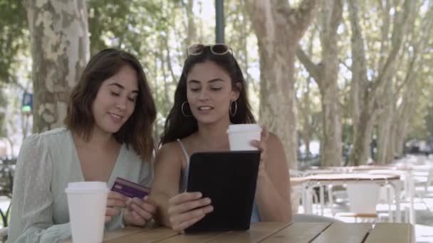 Mujeres jóvenes alegres que pagan con tarjeta de plástico a través de la tableta - Imágenes, Vídeo