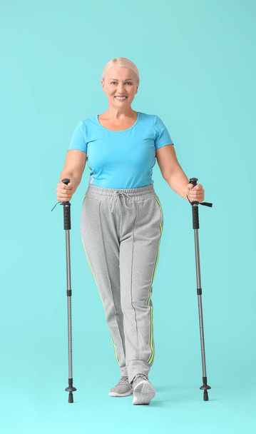 Mature woman with walking poles on color background - Photo, Image