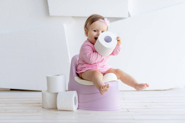 little girl sitting in a white room on a potty in pink clothes with toilet paper - 写真・画像
