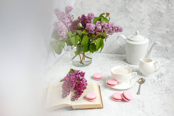 Una tazza di caffè del mattino, una ciotola di lilla, maccheroni, su fondo chiaro. Cartolina buongiorno - Foto, immagini
