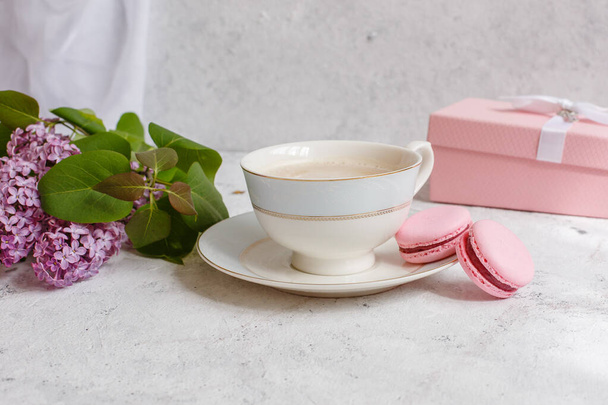 Ένα φλιτζάνι πρωινό καφέ, ένα μπολ λιλά, μακαρόνια, σε ελαφρύ φόντο. Ταχυδρομική κάρτα καλημέρα - Φωτογραφία, εικόνα