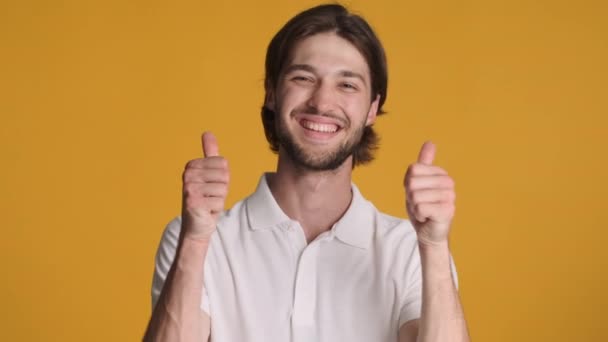 Atrakcyjny wesoły facet pokazuje kciuki przed kamerą i uśmiecha się na kolorowym tle. Jak ekspresja - Materiał filmowy, wideo