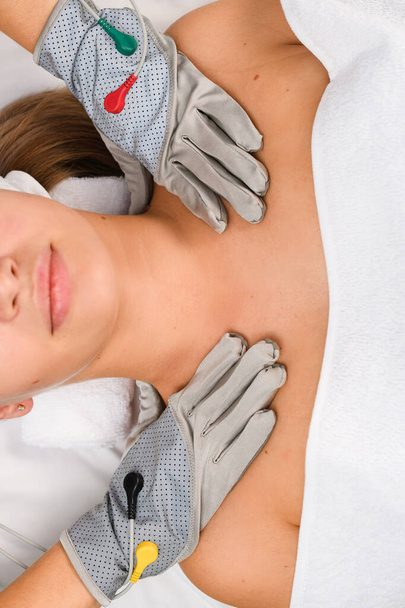 Il cosmetologo di hardware in guanti microcorrenti grigi per terapia di miostimolazione mette mani su spalle di cliente femminili, su vista. - Foto, immagini