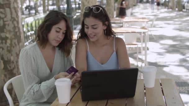 Giovani amiche sedute in città caffè e utilizzando il computer portatile - Filmati, video